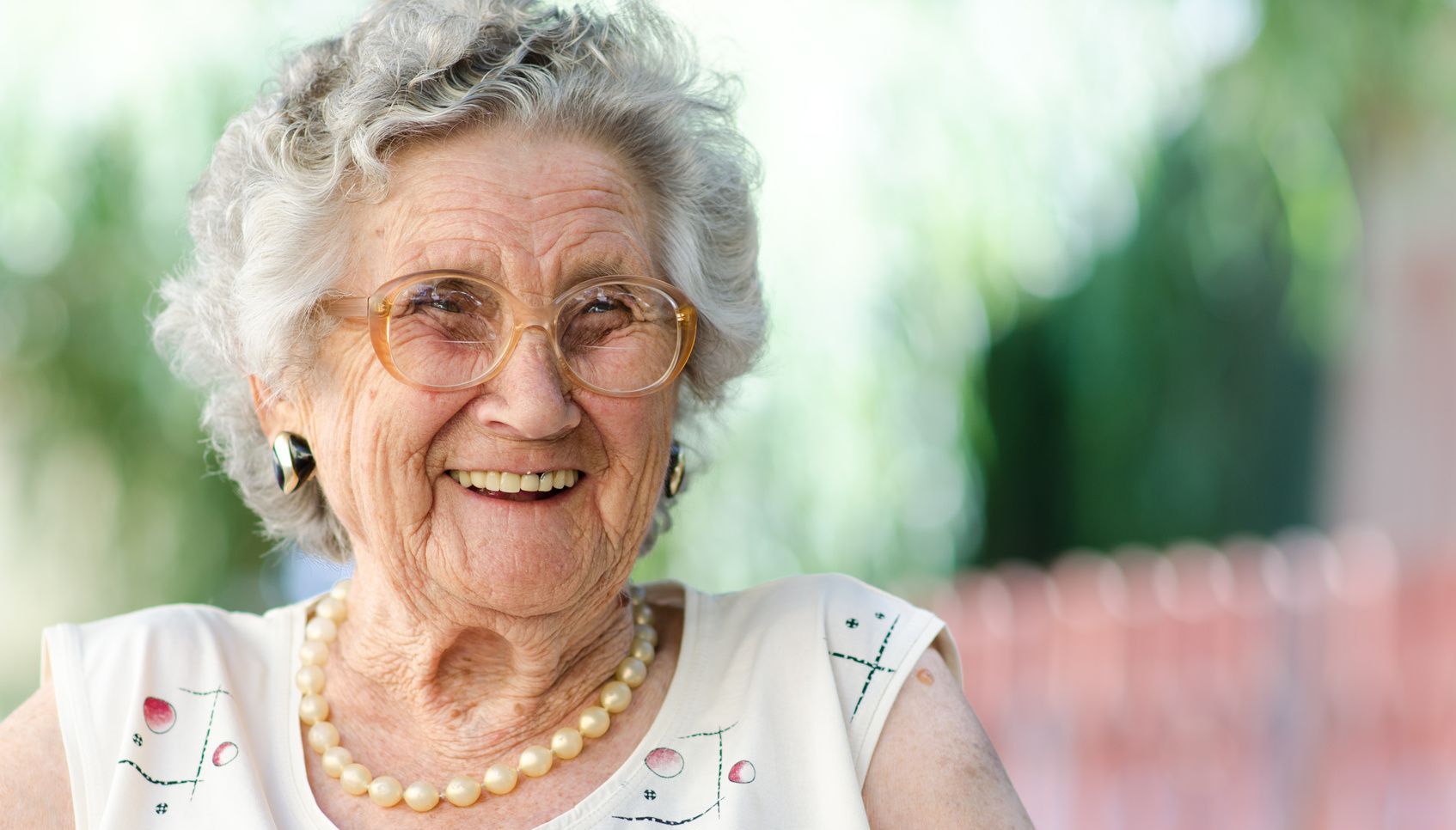 an elderly woman wearing glasses and a pearl necklace is smiling .