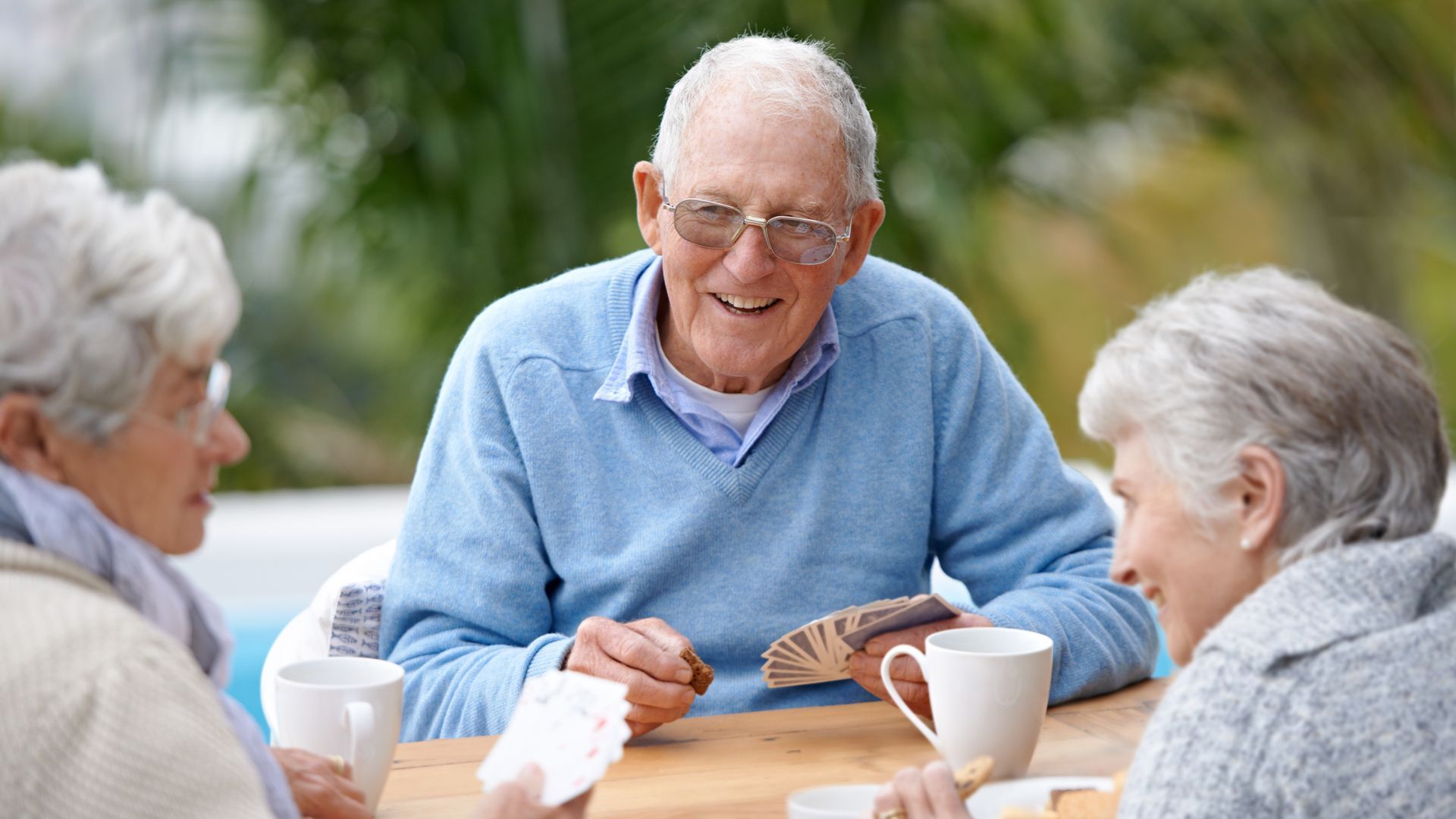 a group of elderly people are sitting at a table playing cards .