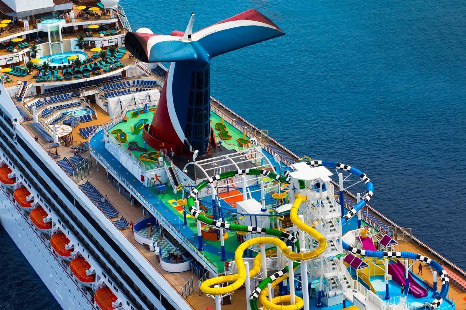 Cruise ship deck with waterslides and pools, against a blue ocean backdrop.