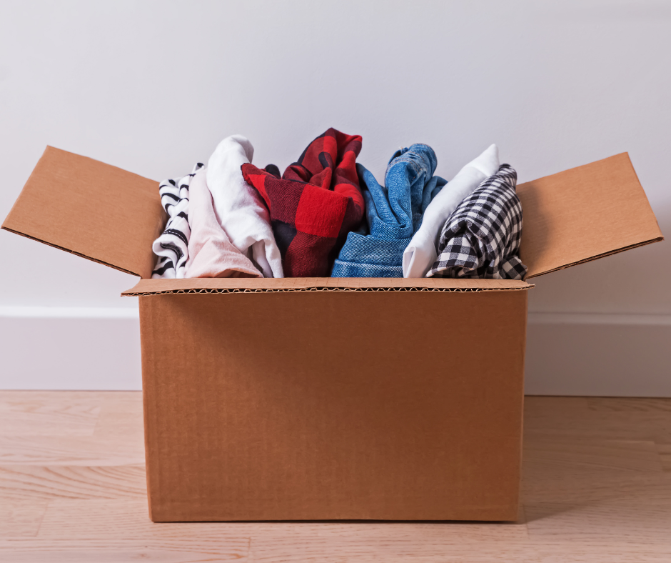 Open cardboard box filled with folded clothes in white, red, blue, and black patterns on a floor
