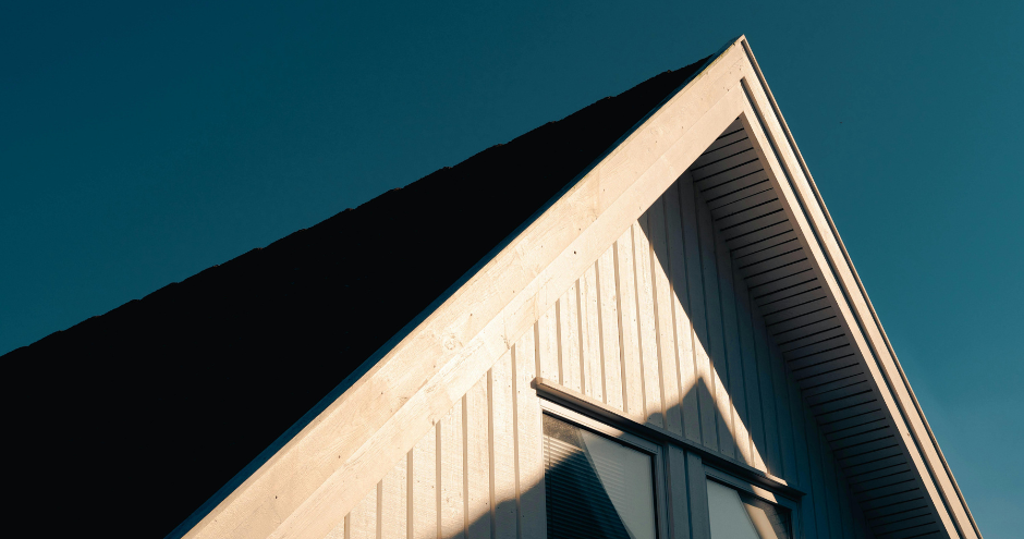 Modern house roof and gable with white siding against a deep blue sky