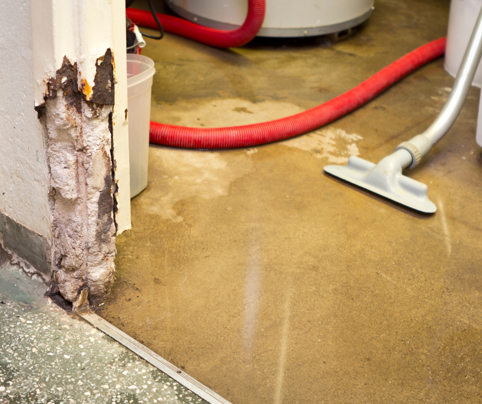Damaged wall with water damage on a concrete floor next to a vacuum. Red hose and bucket in the background.