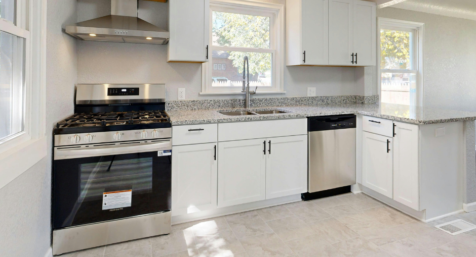 A modern kitchen featuring white cabinets, stainless steel appliances, and grey speckled countertops.