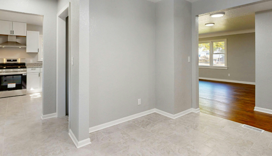 Interior view: Entryway with light gray walls, kitchen to the left, living room to the right, and light flooring.
