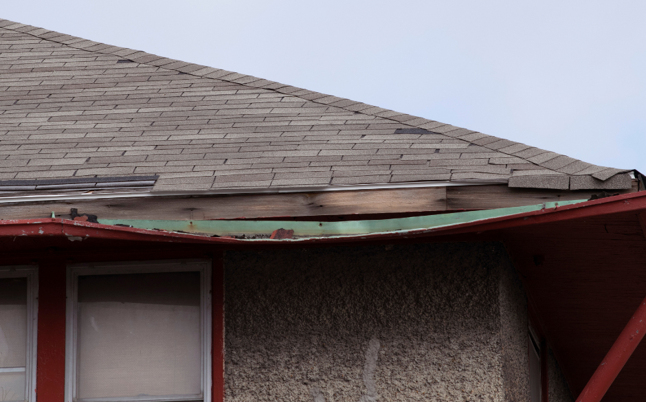 Damaged roof shingles on a building with visible underlayment and a red trim.
