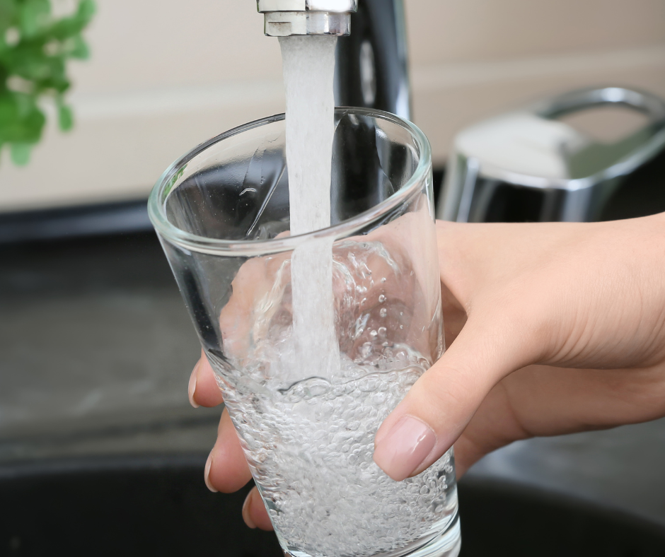 Water flowing from a faucet into a clear glass held in someone's hand over a sink.