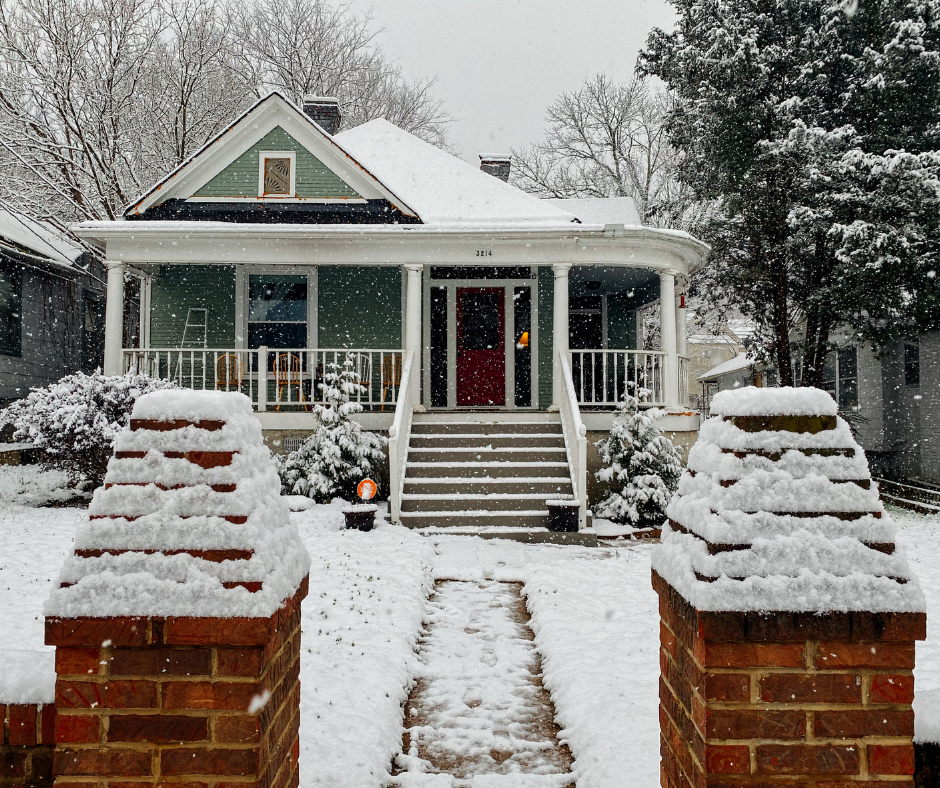 Snow-covered house with porch and brick gateposts in winter, with a walkway leading to the front door.