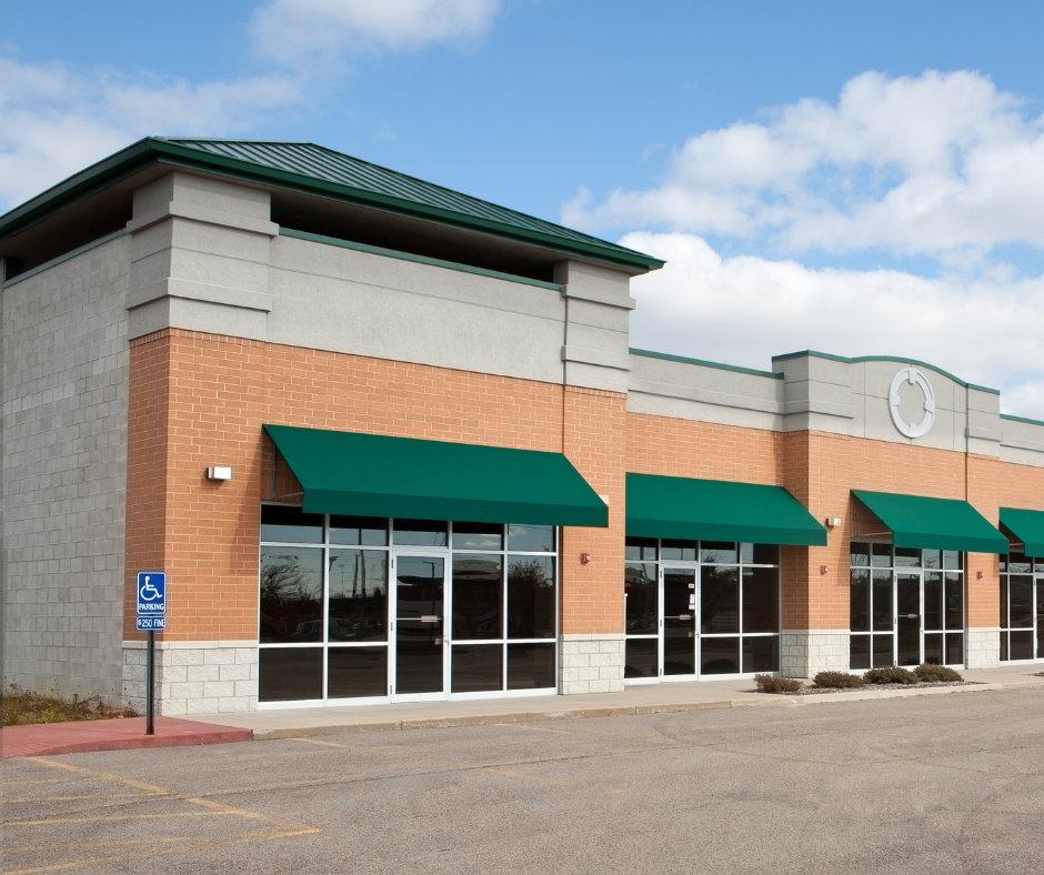 Storefront strip mall with green awnings and brick-and-beige facade on an empty parking lot