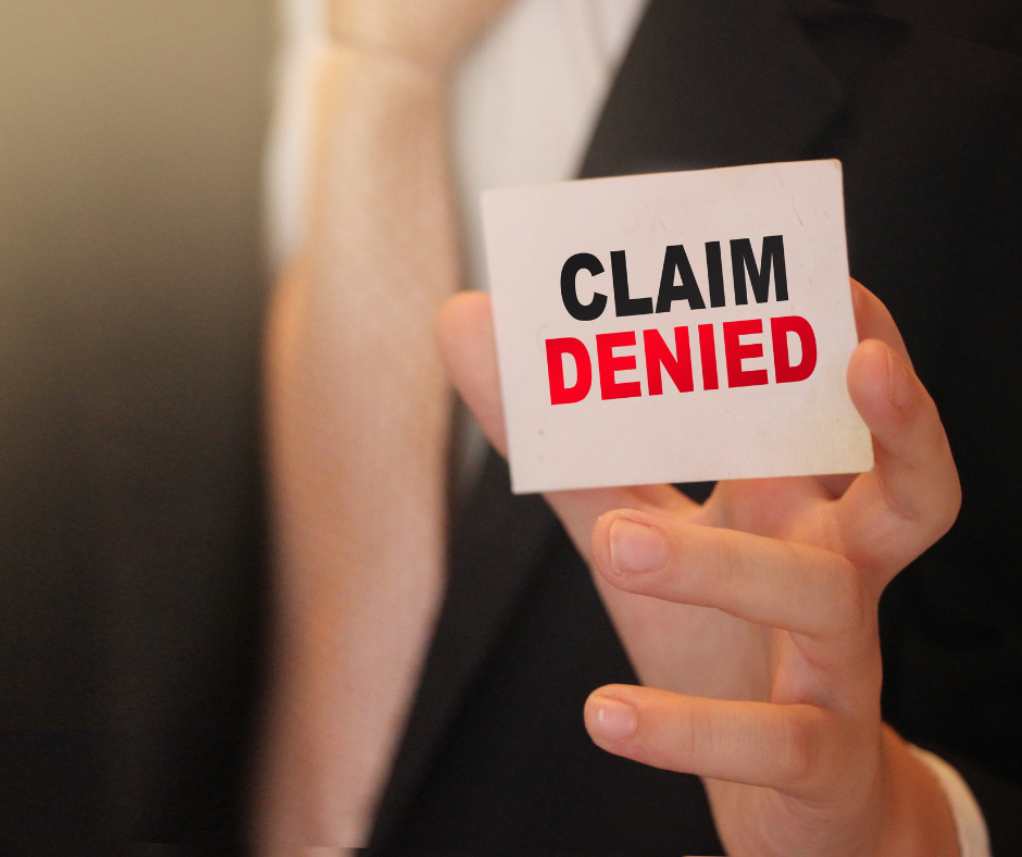 Hand holding a card reading “CLAIM DENIED” in black and red text