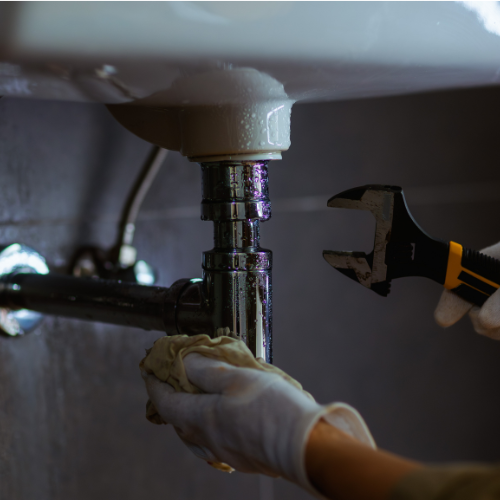 Gloved hands using a wrench to repair a sink drain pipe under a bathroom sink
