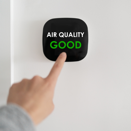 Hand pointing at black air quality monitor displaying “GOOD” in green text