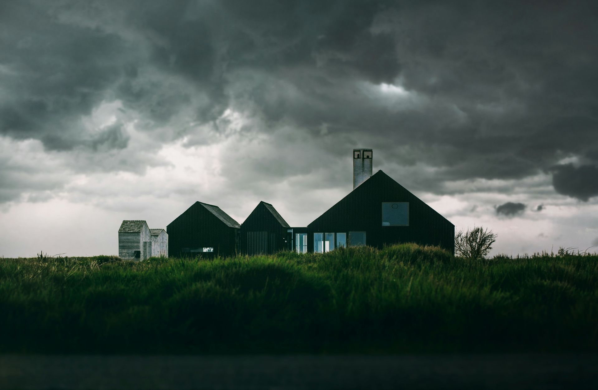 A black house is sitting on top of a grassy hill under a cloudy sky.