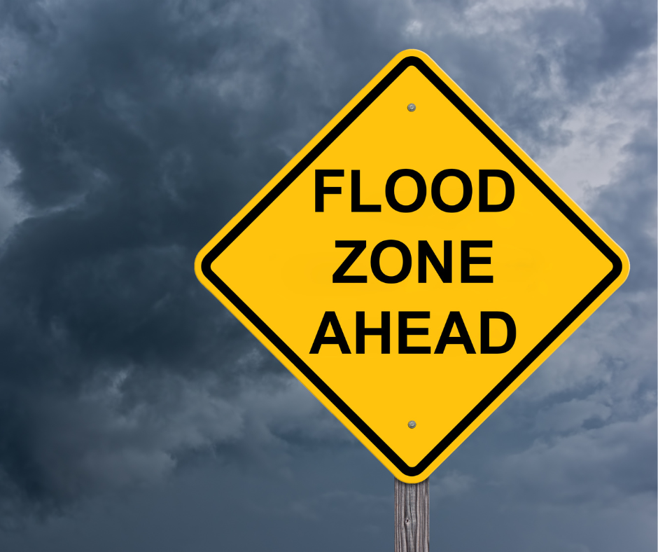 Yellow flood zone warning sign against a dark, stormy sky.