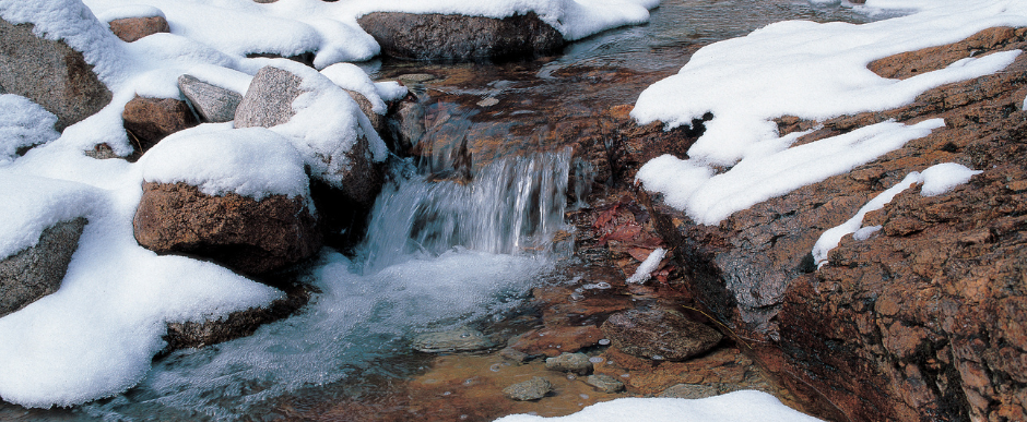 Snowy rocks border a flowing stream of water.