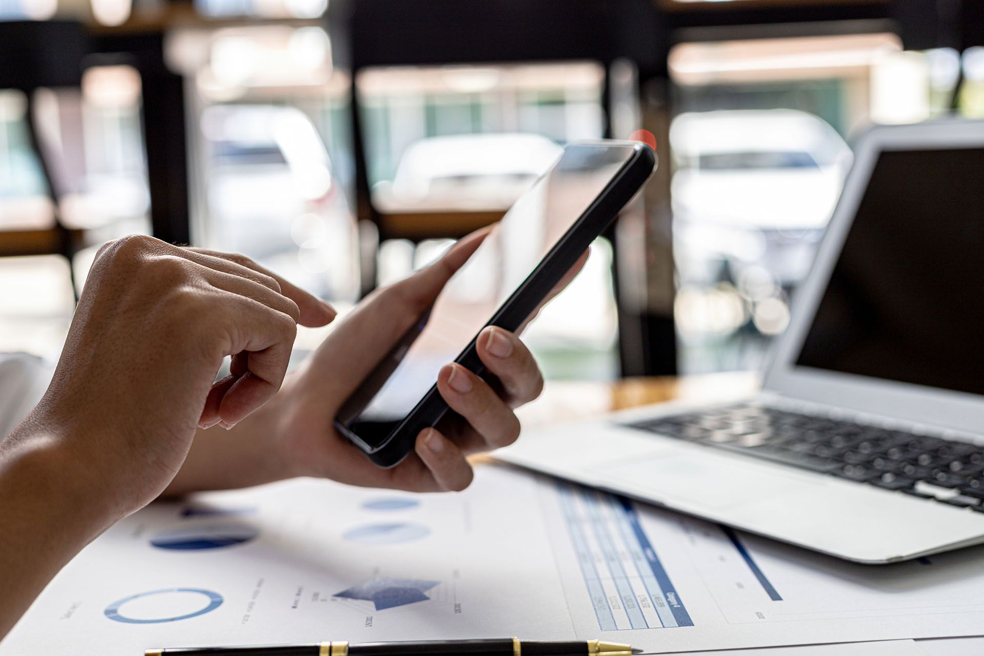 A person is using a cell phone in front of a laptop.