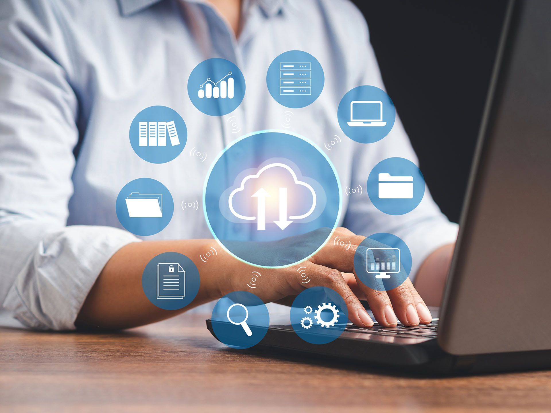A person is typing on a laptop computer with a cloud surrounded by icons.