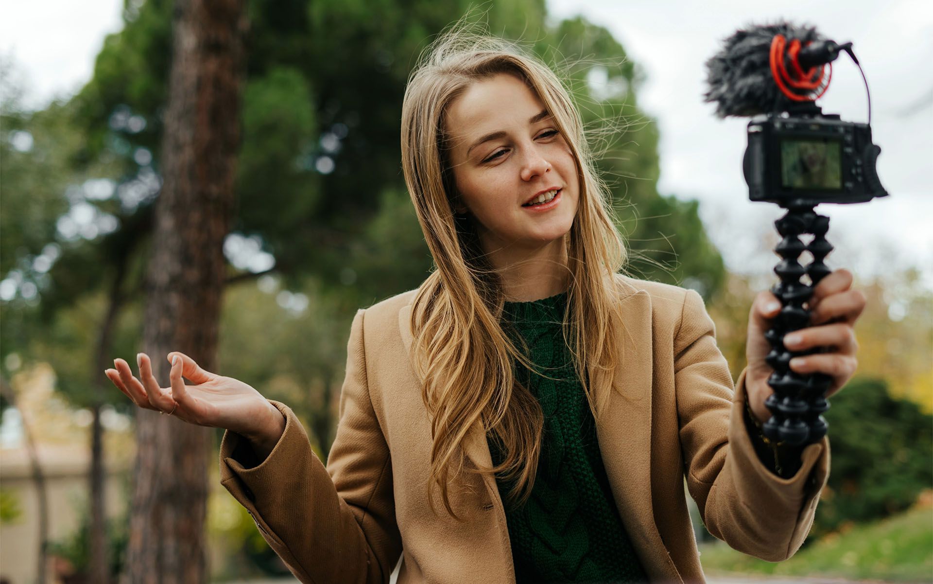 A woman is holding a camera on a tripod and talking into it.