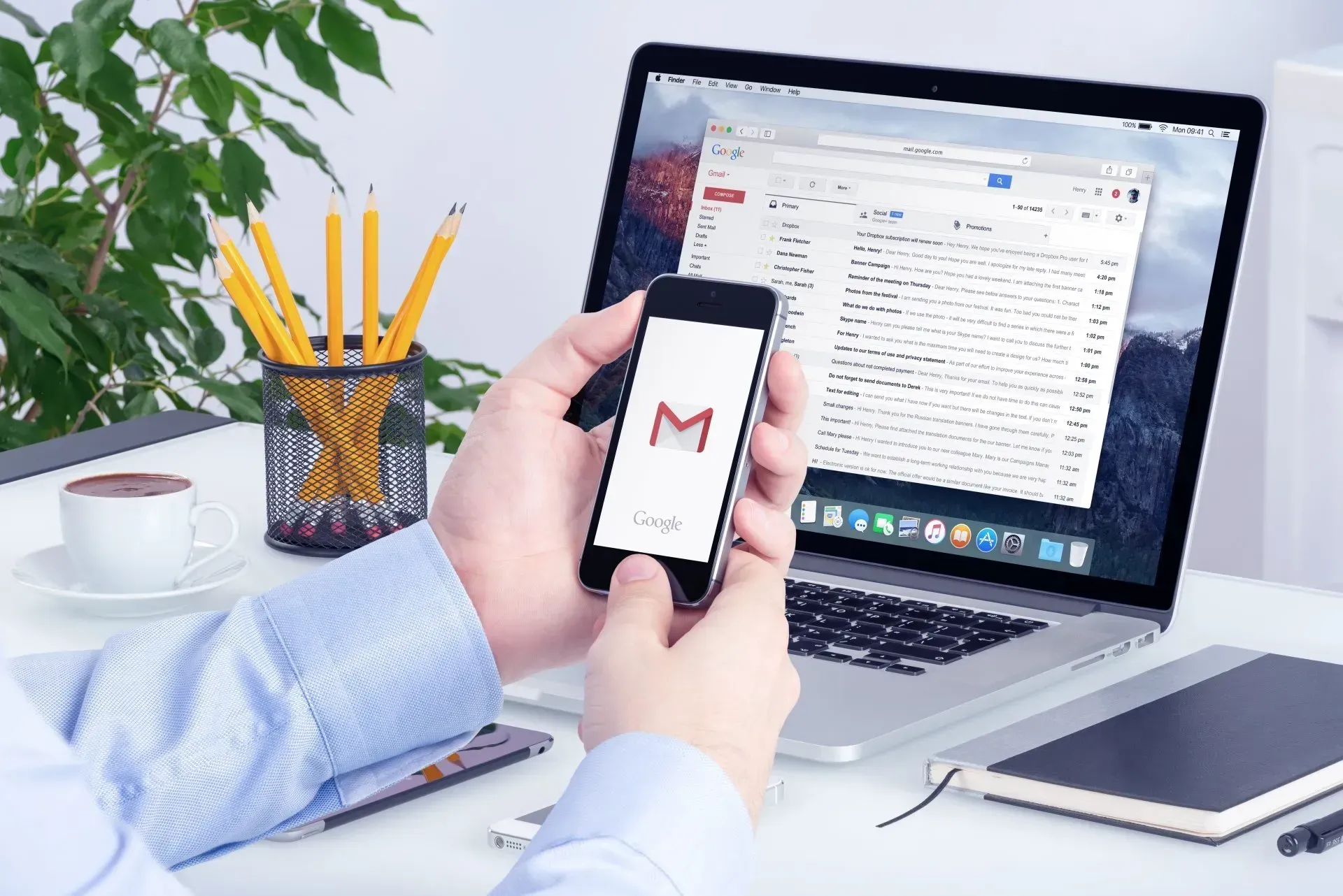 A person is holding a cell phone in front of a laptop using Gmail as part of a Google Workspace CRM