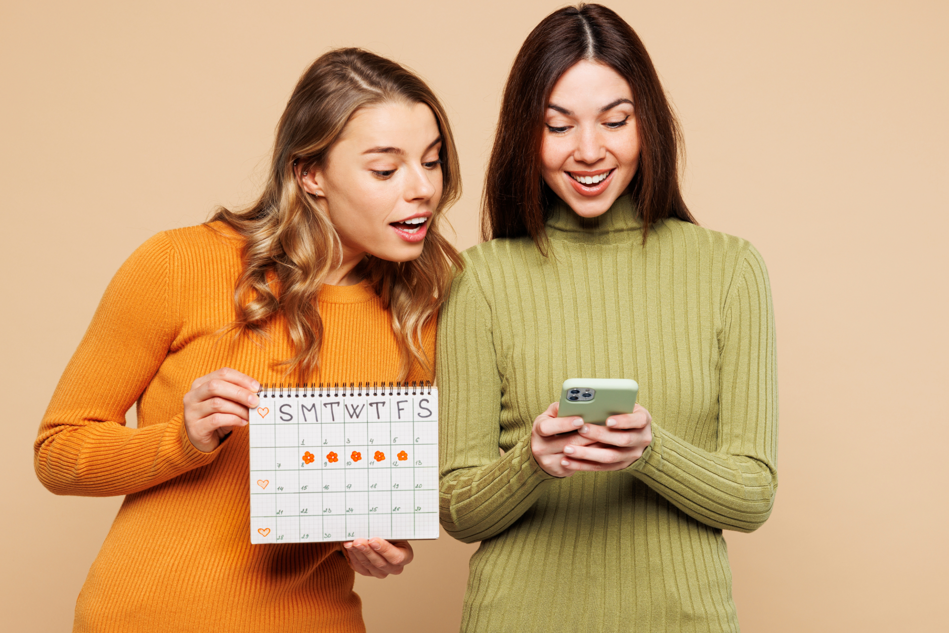 Two women looking at the calendar and phone, one surprised, one smiling.