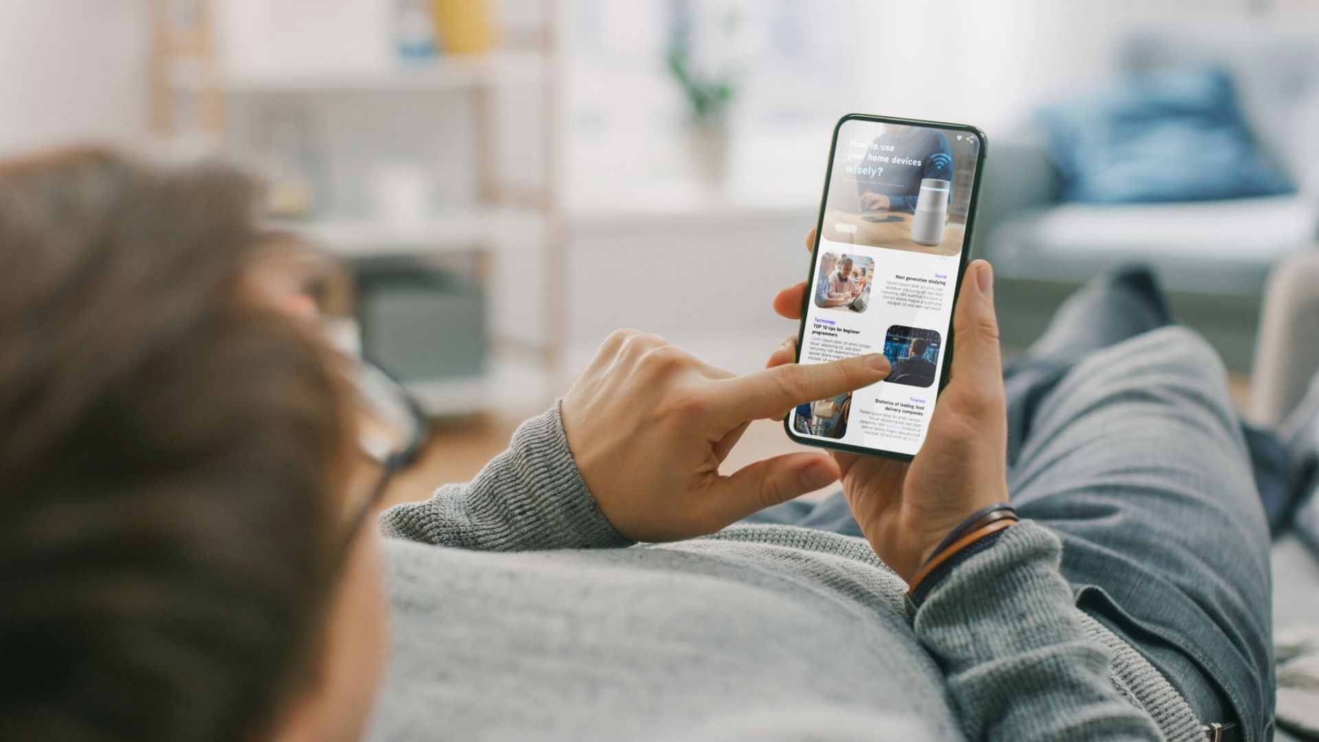 Person lying on a couch browsing a smartphone; the screen shows product images.