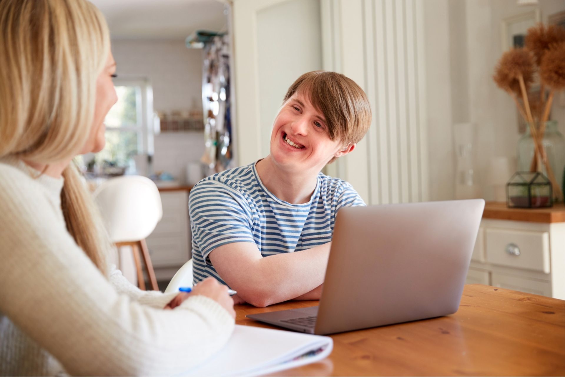 Woman and man with Down syndrome at a table with laptop, smiling and talking.