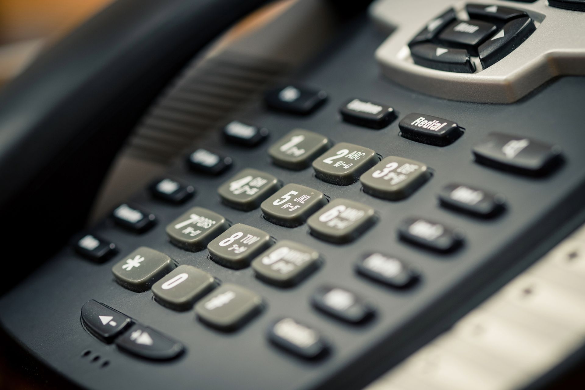 Close-up of a dark gray office phone with multiple buttons, including number keys and function buttons.