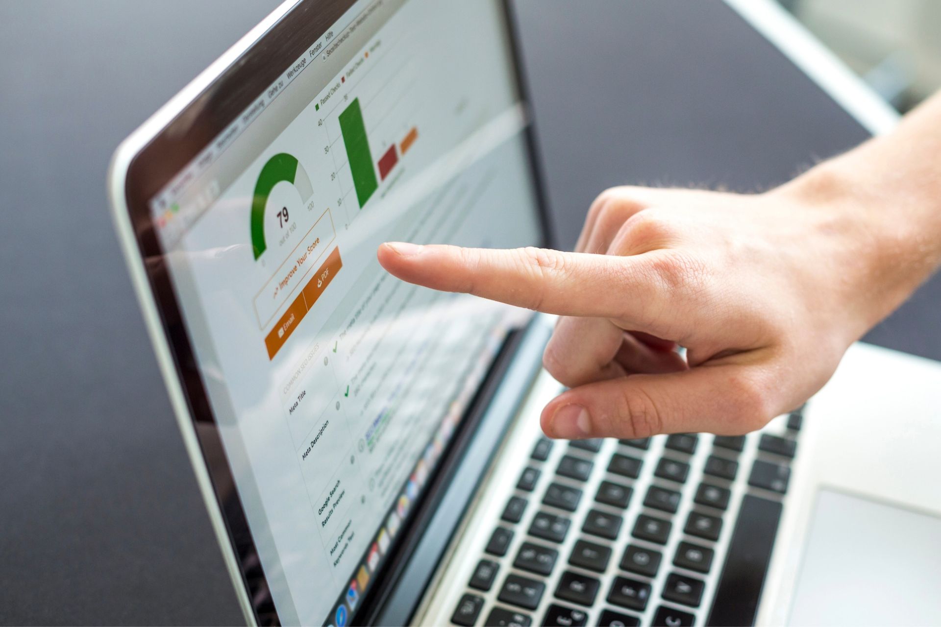 Hand pointing at a laptop screen displaying charts and graphs, likely analytics.
