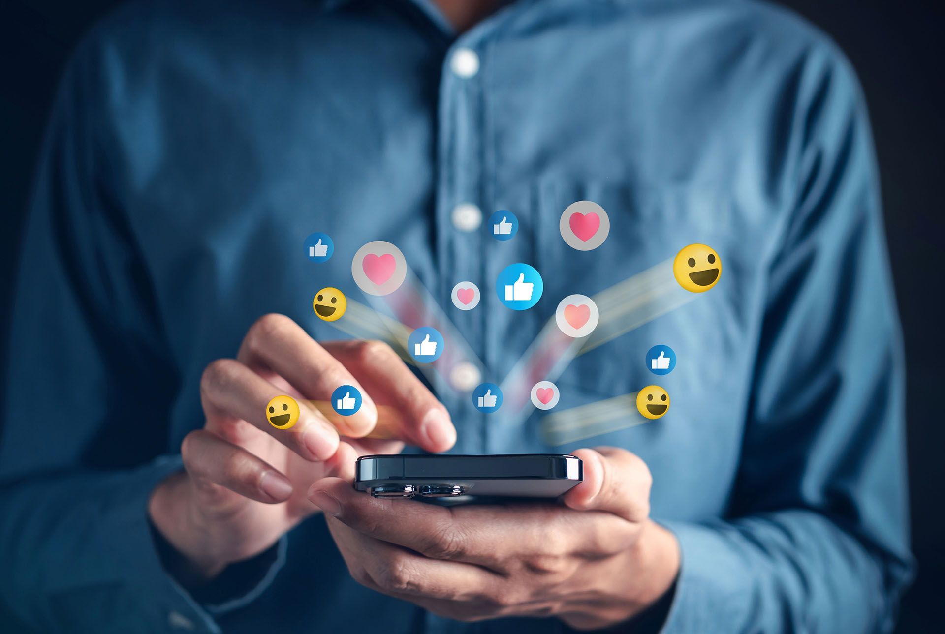 A person is holding a cell phone in their hand with social media icons coming out of it.