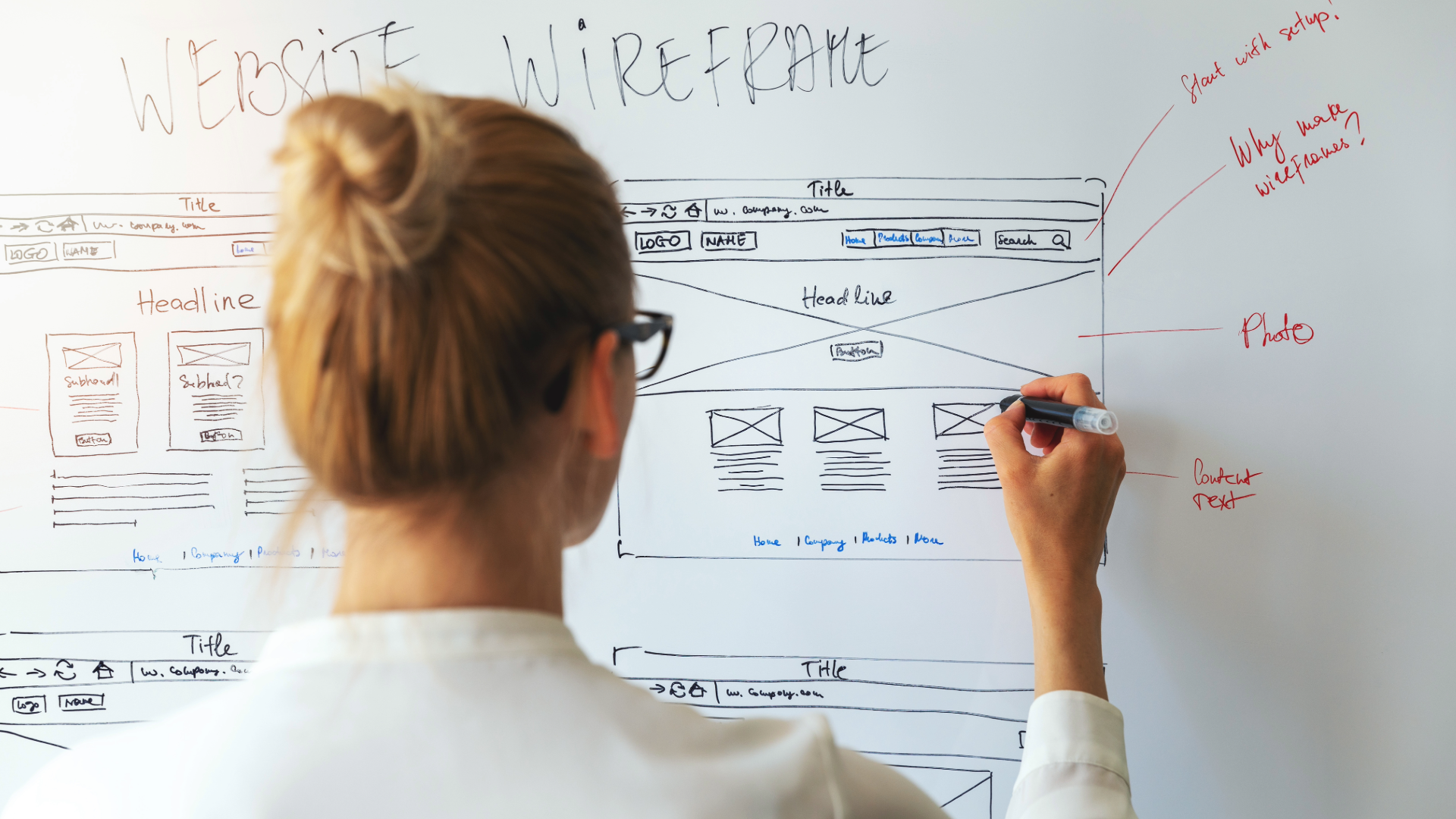 Person writing on a whiteboard filled with diagrams and notes in a bright office