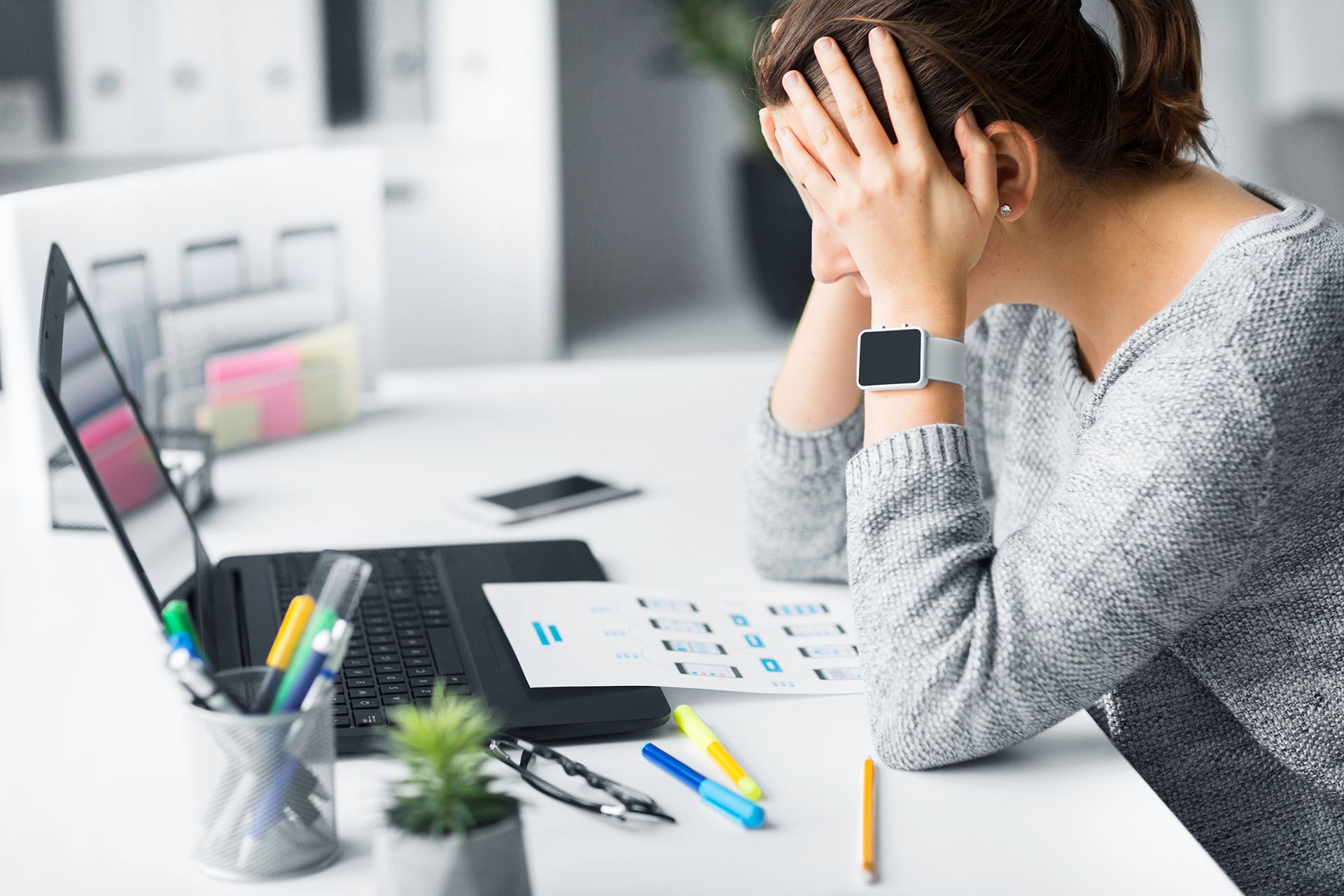 A woman is sitting at a desk with her head in her hands.
