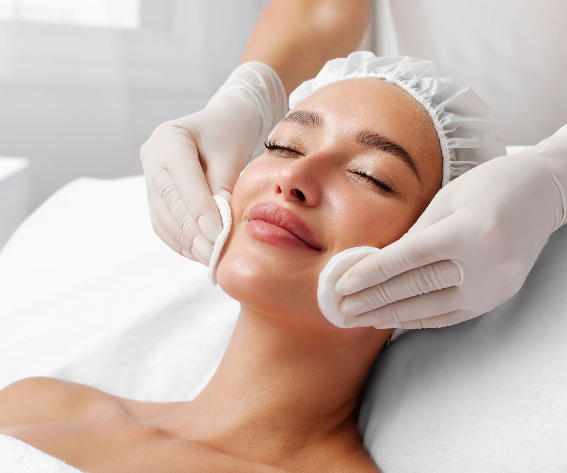 Woman receiving facial treatment, being cleaned with cotton pads, relaxing.