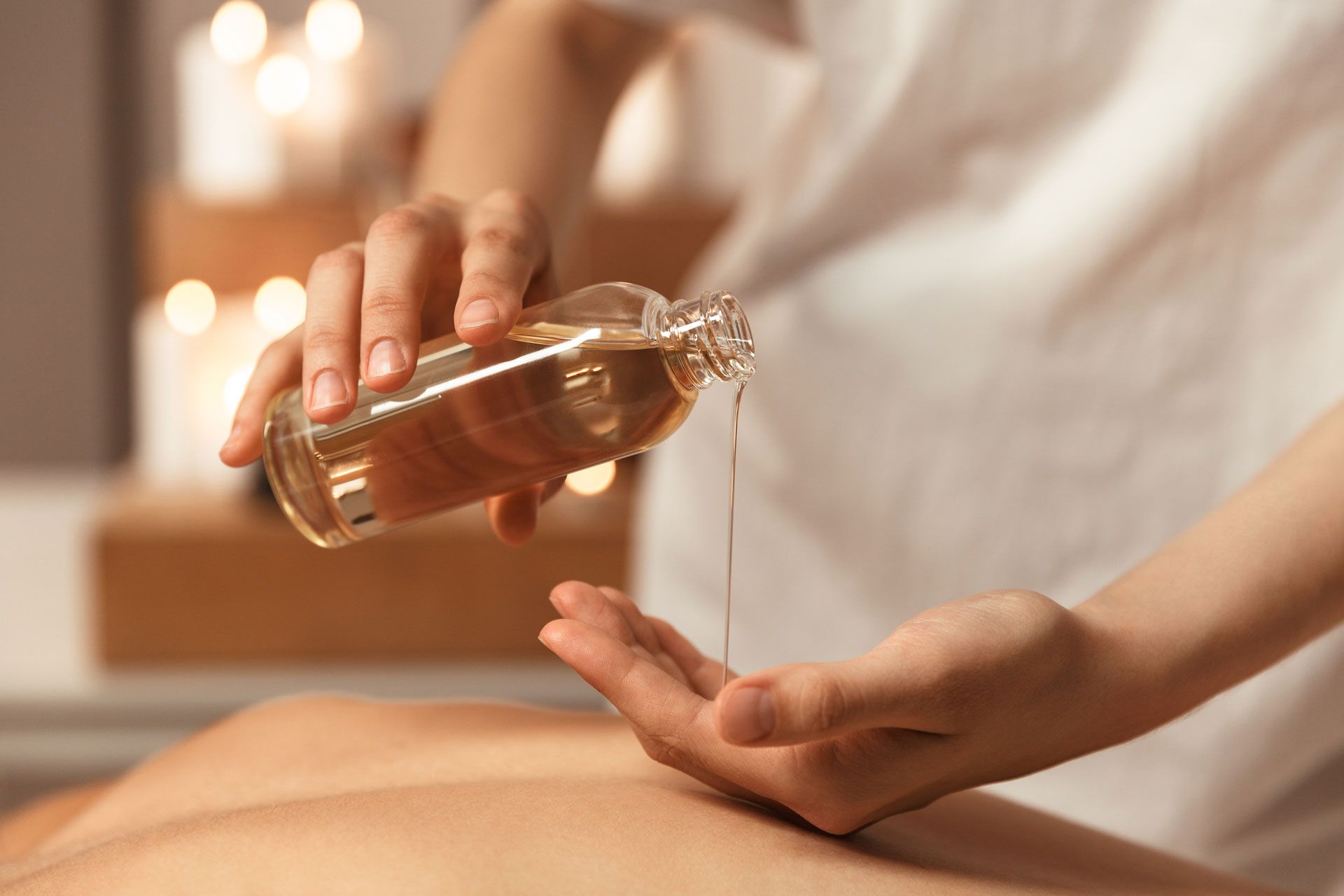 Person pouring massage oil onto their hand, preparing for a massage in a candlelit room.