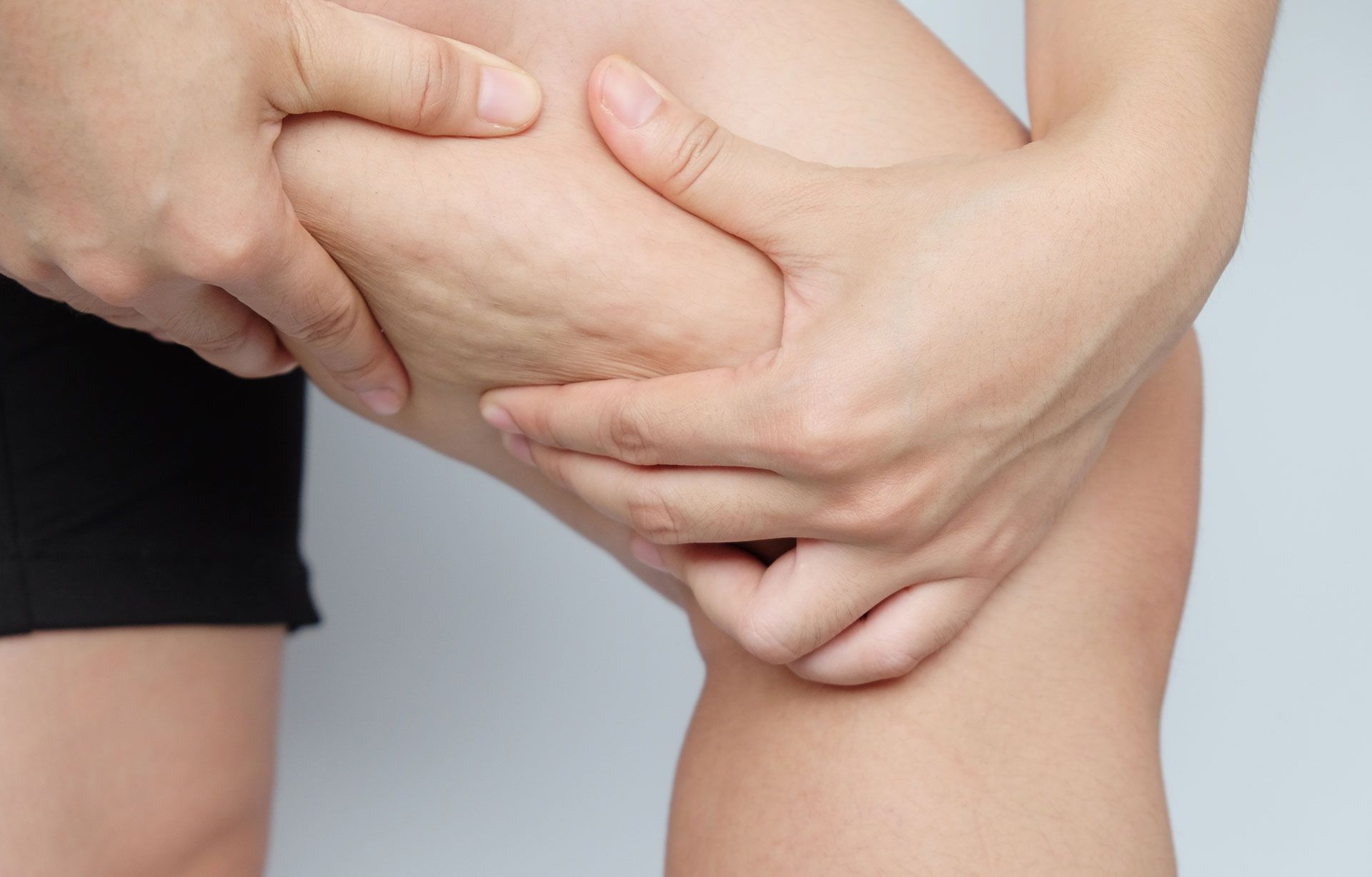 Hands pinching thigh, showing dimpling of skin, possibly cellulite.