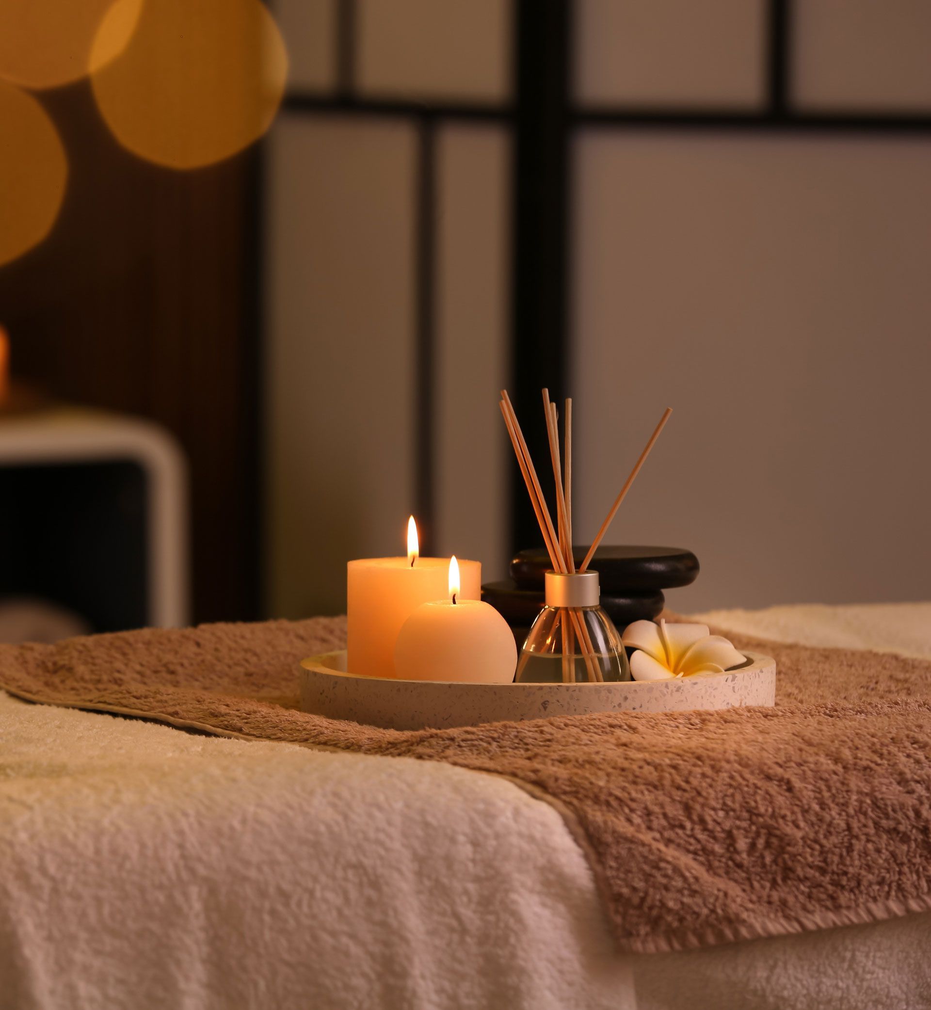 Candles, essential oil diffuser, and flowers on a massage table. Spa-like setting.