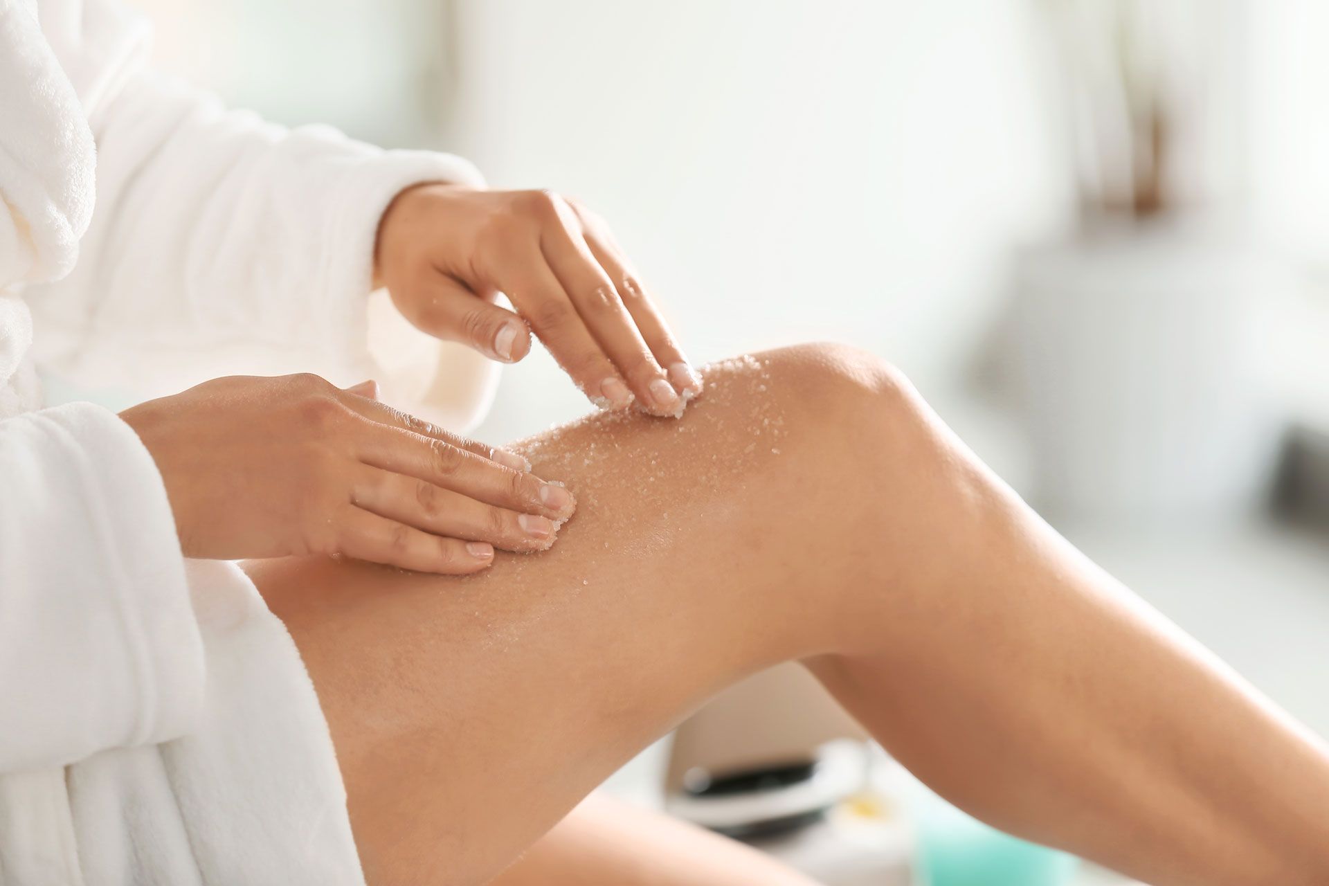 Person in bathrobe applying body scrub to leg.