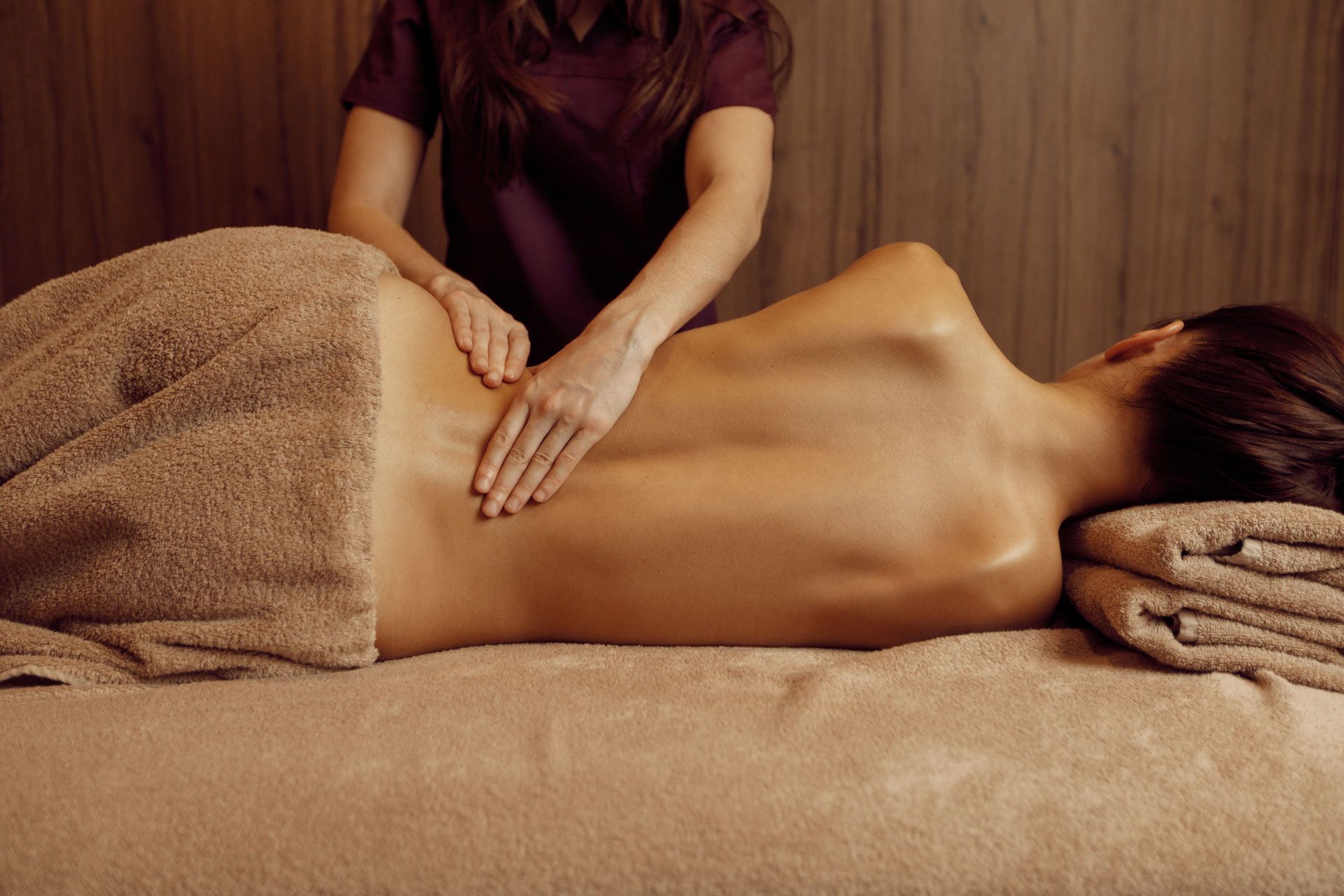 Woman receiving back massage, therapist's hands on lower back, covered in towel, on massage table.