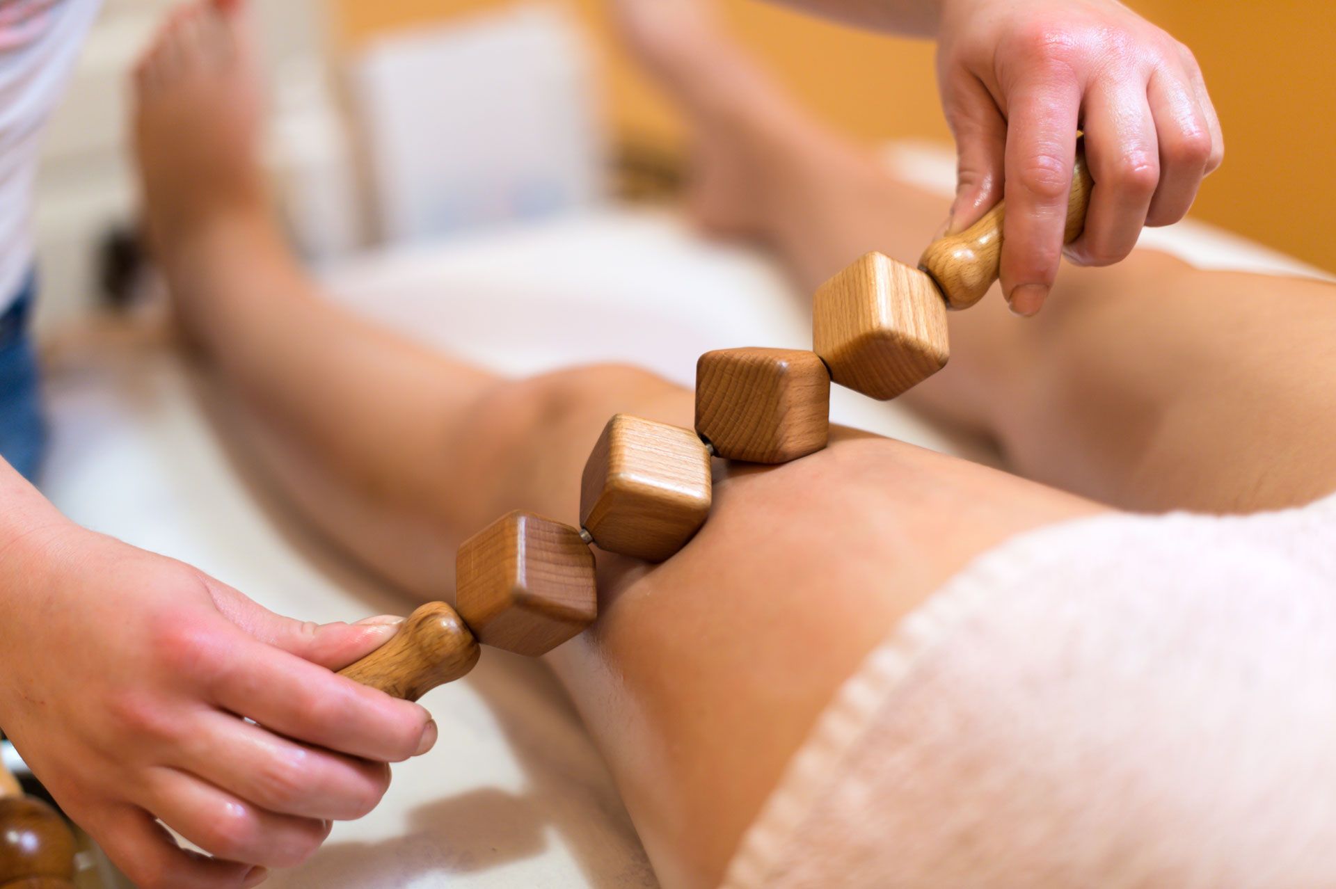 Leg massage with wooden rolling tools on a person's thigh, indoor setting.