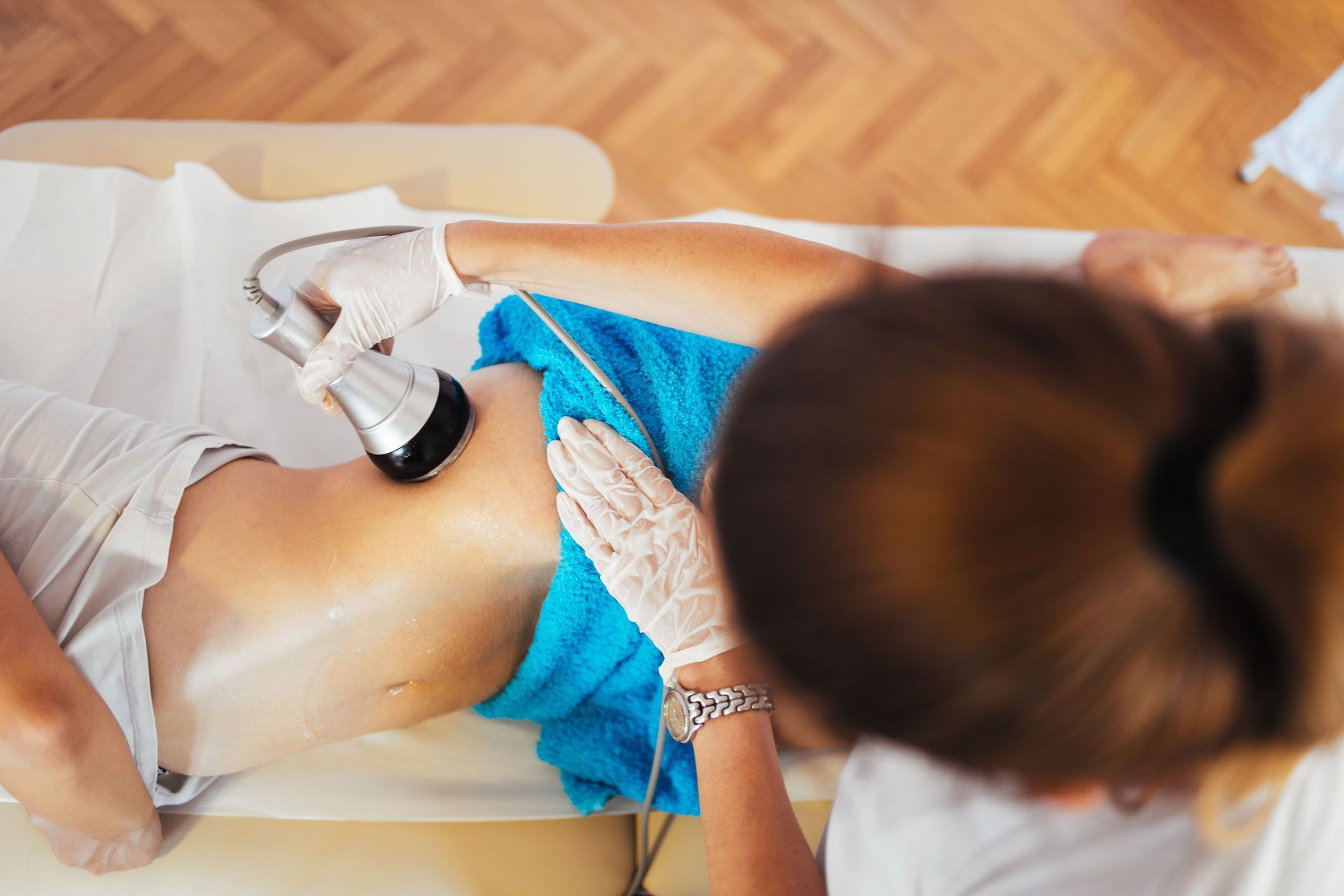 Person receiving abdomen treatment with device by gloved hands, lying on a table.