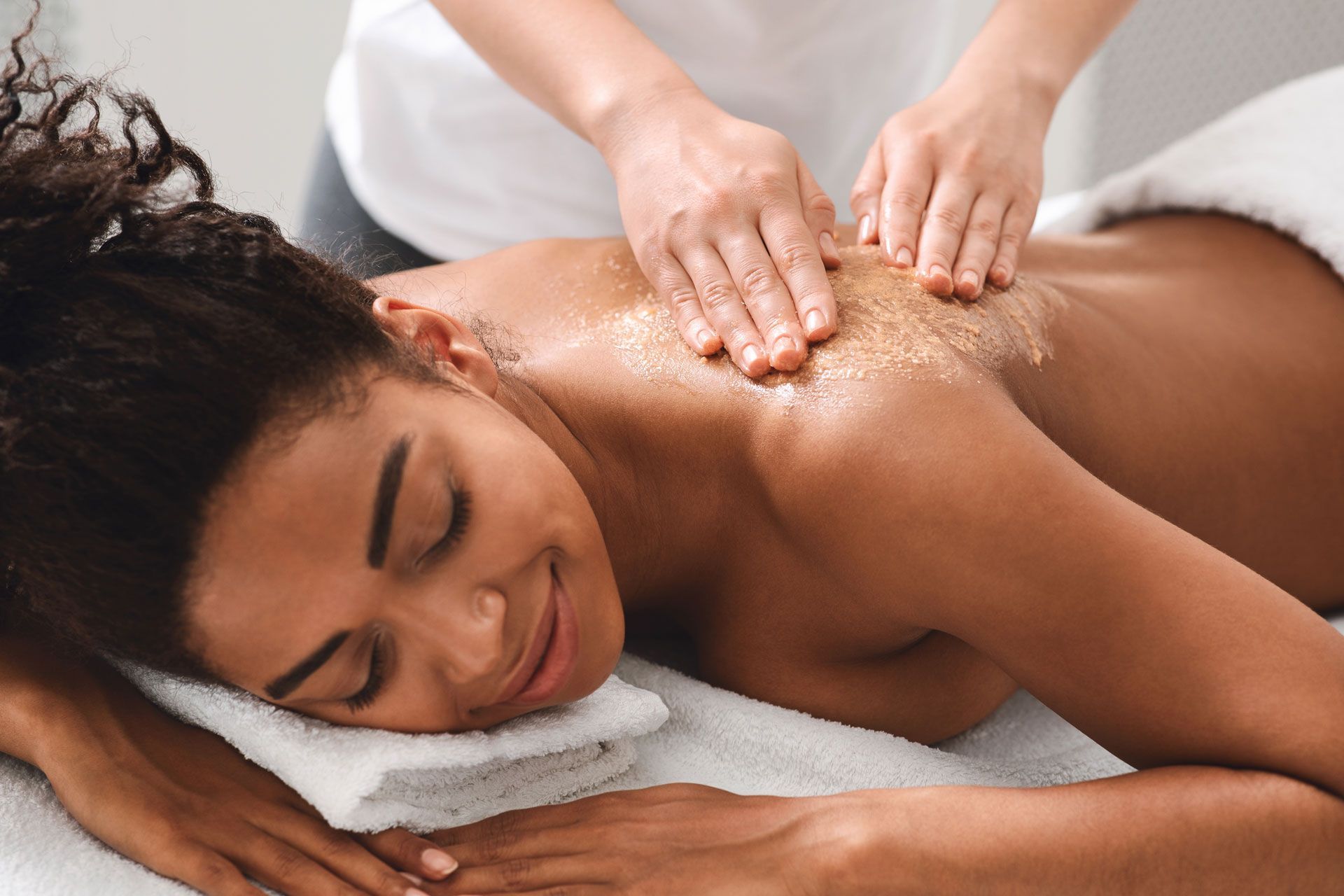 Woman receiving back scrub at spa, smiling.