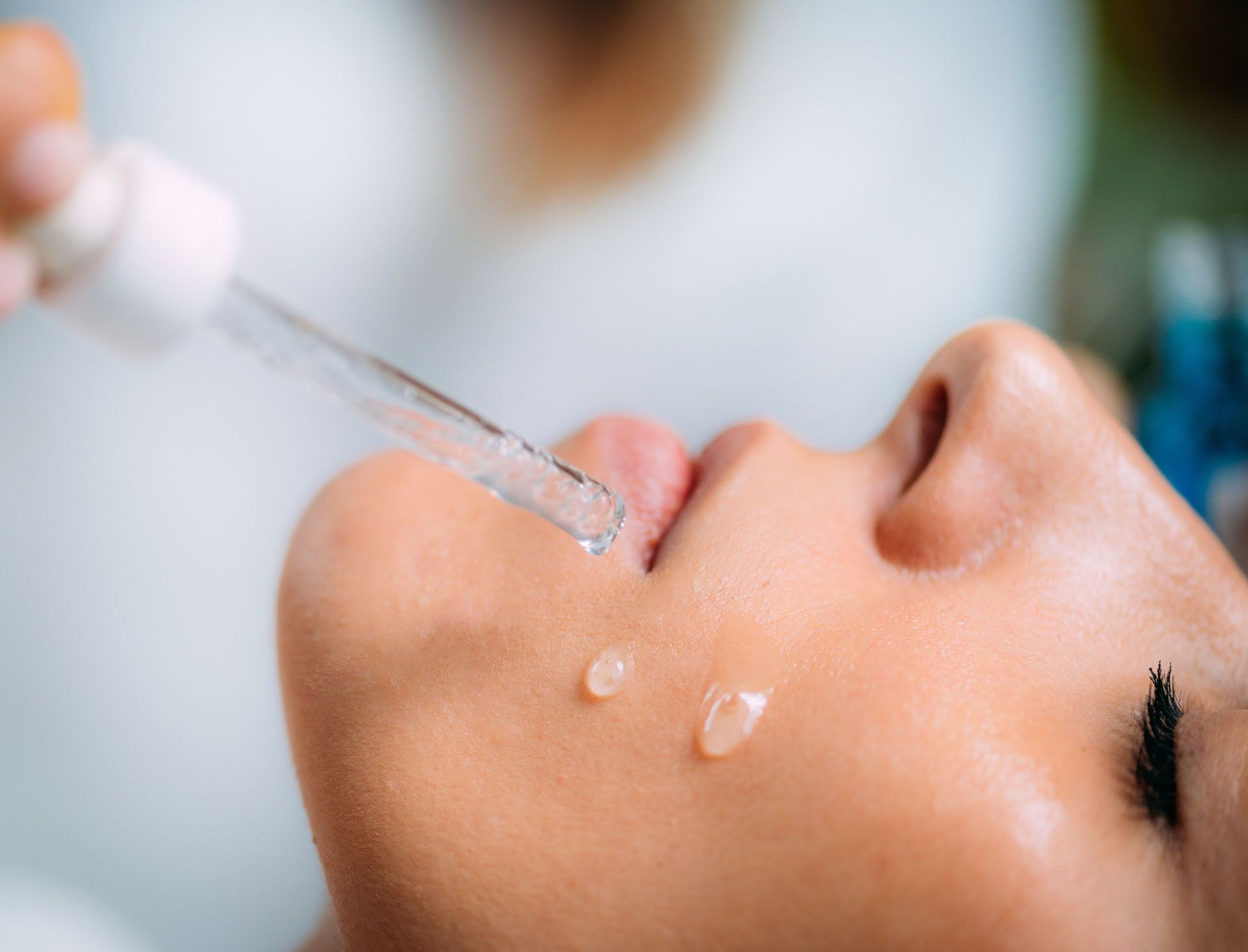 Close-up of a person's face with a dropper dispensing liquid onto their skin.