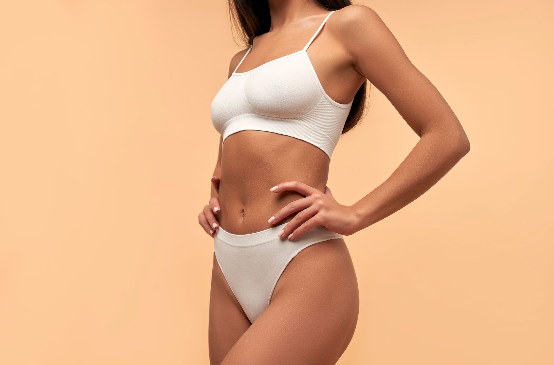 Woman in white underwear and crop top, hands on hips, beige background.