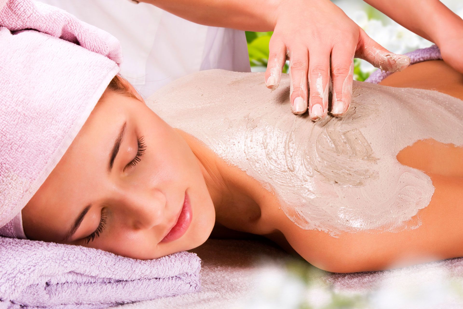 Woman receiving a mud spa treatment on her back; lying down with eyes closed, hands of another person applying mud.
