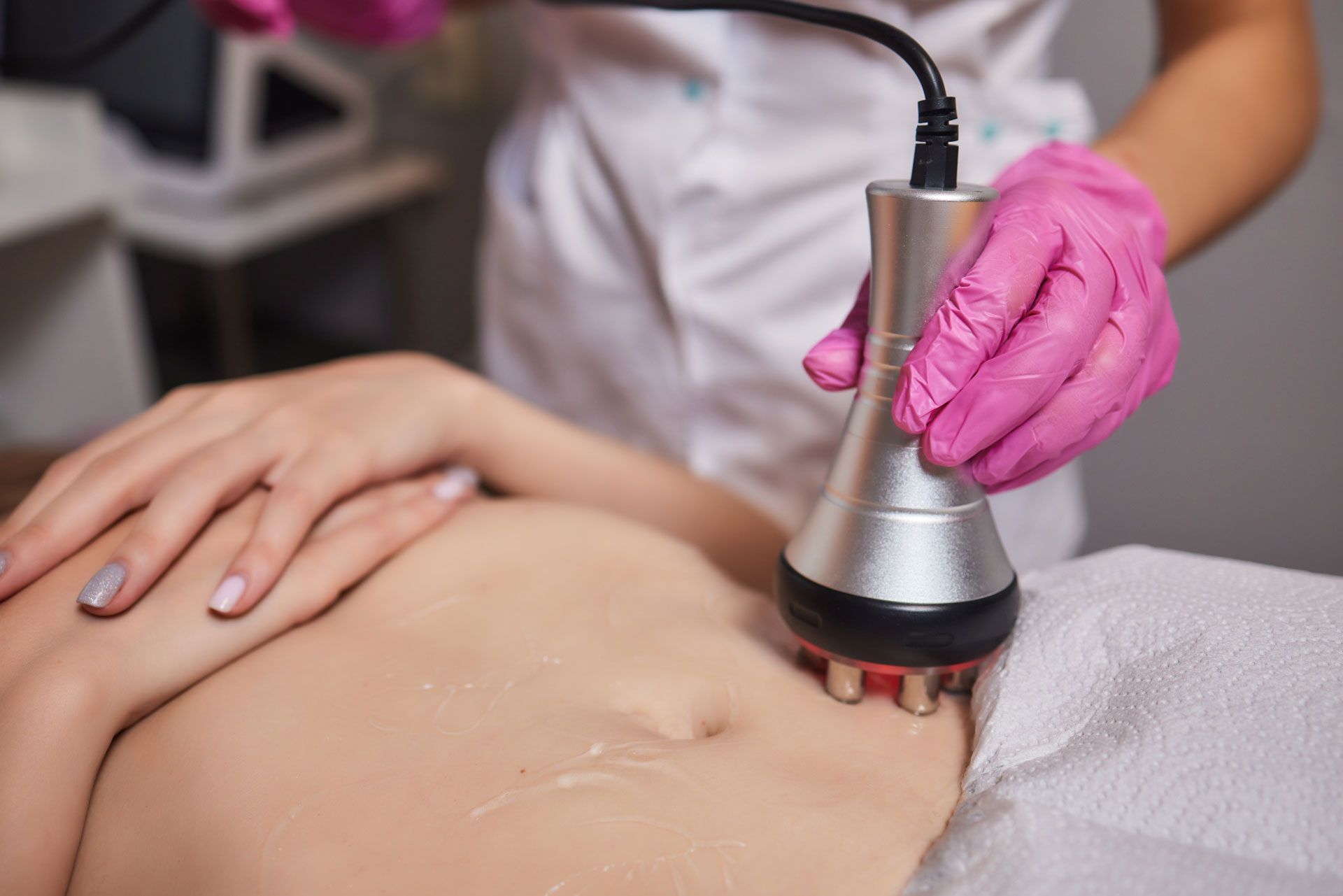 Person receiving a body treatment. A technician wearing pink gloves uses a device on the abdomen.