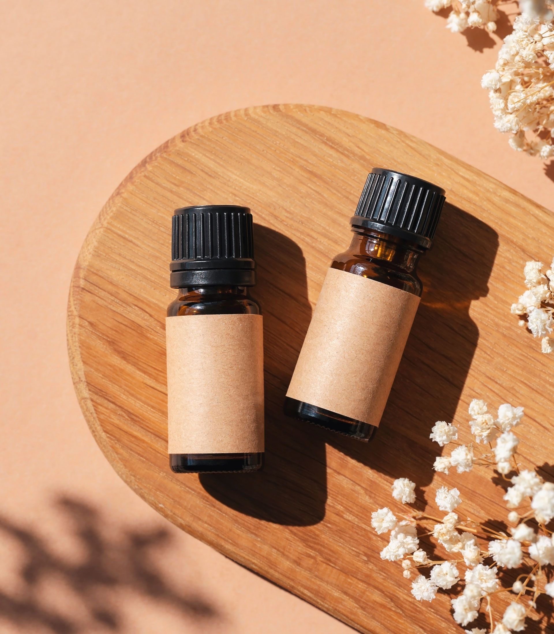 Two amber essential oil bottles with blank labels on a wooden tray, surrounded by dried flowers.