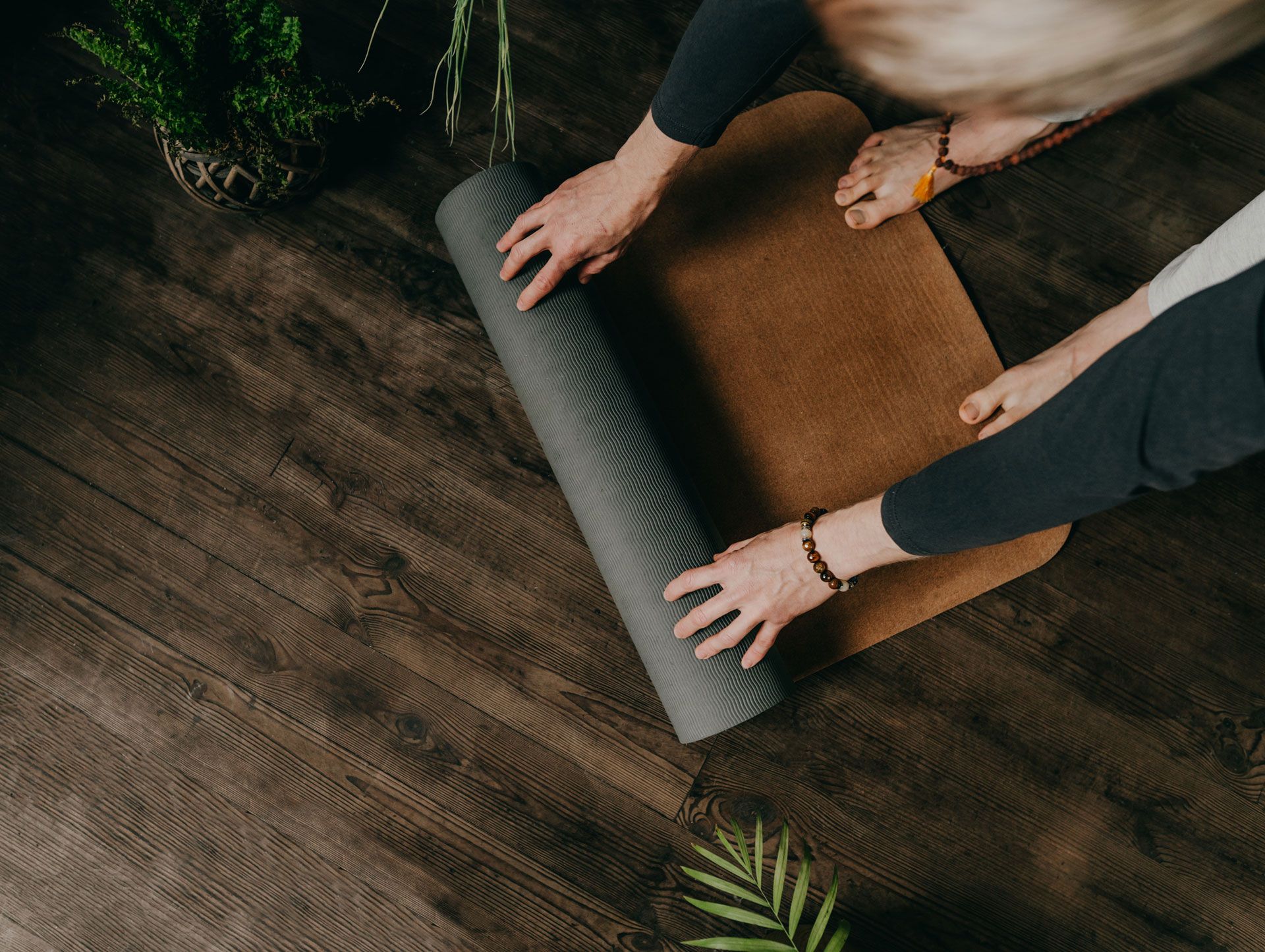 Person rolling out a yoga mat on a wood floor, near plants.