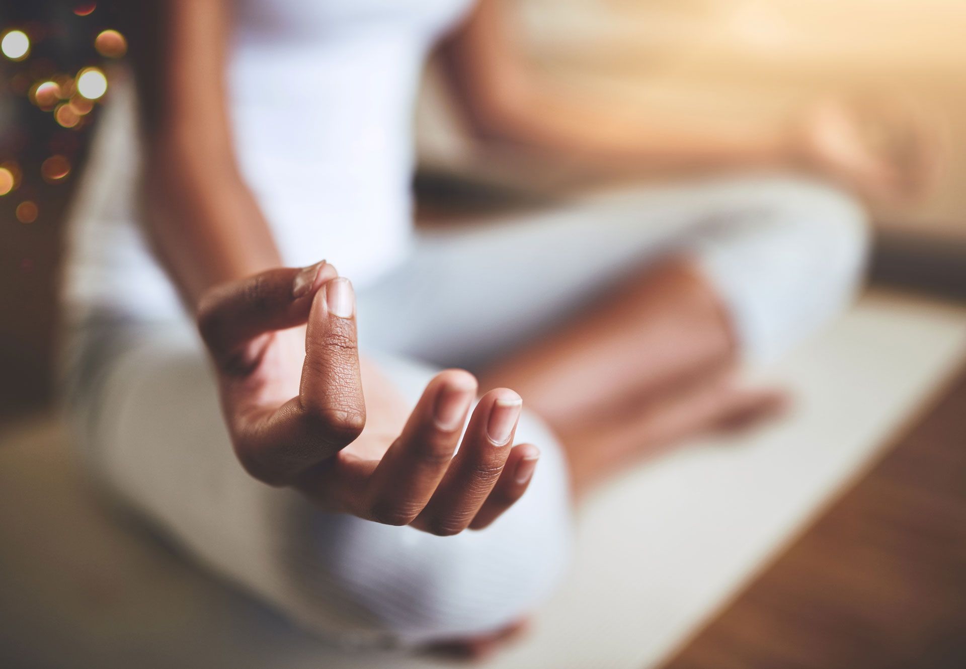 Person meditating with hands in a mudra, in a well-lit room.