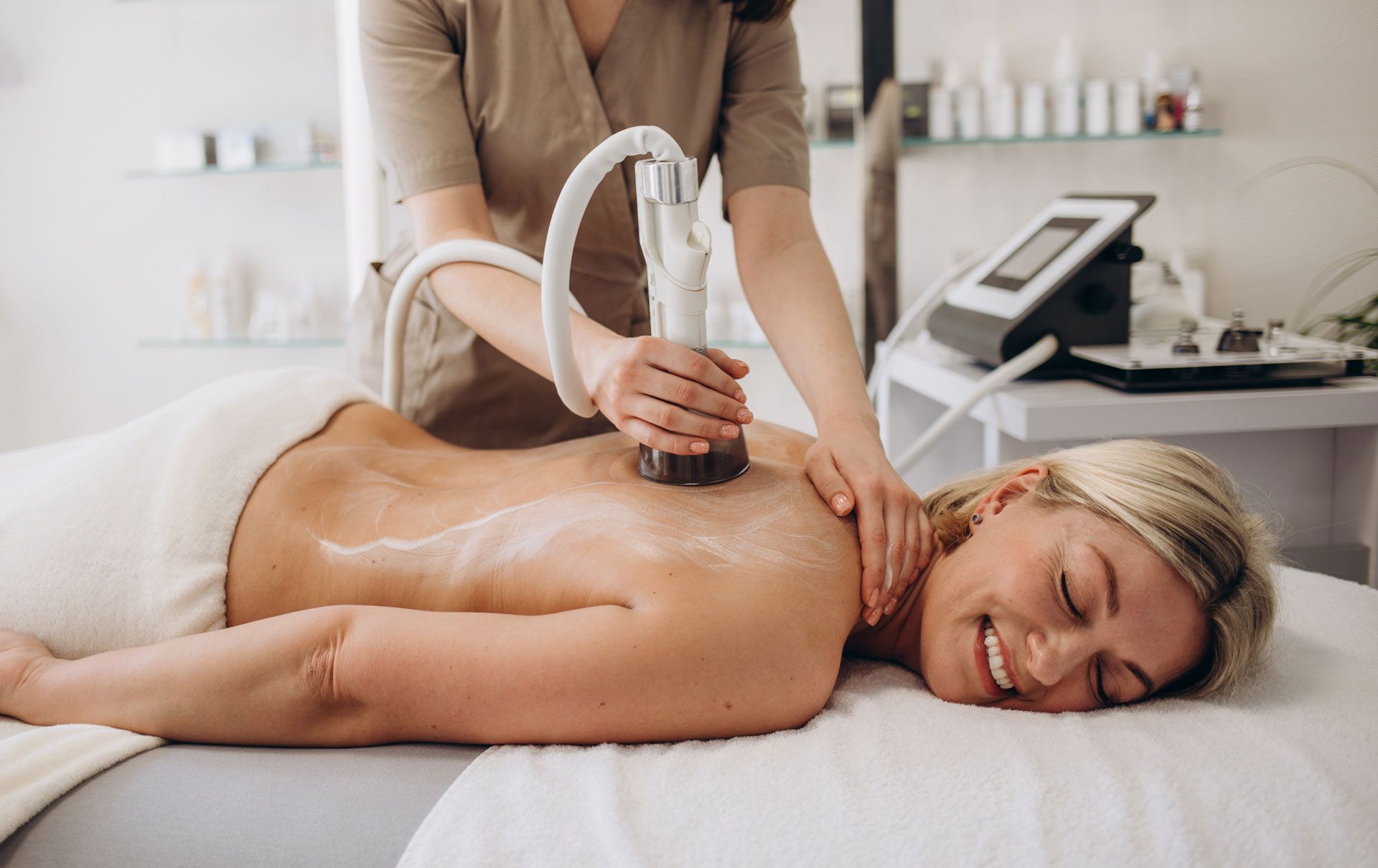 Woman receiving a back treatment with a device in a spa setting. She smiles as the technician works.
