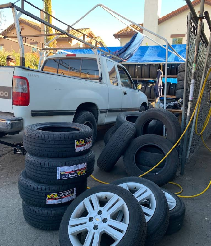 A white pickup truck parked next to stacks of tires and wheels outside a building, with more tires visible on racks.