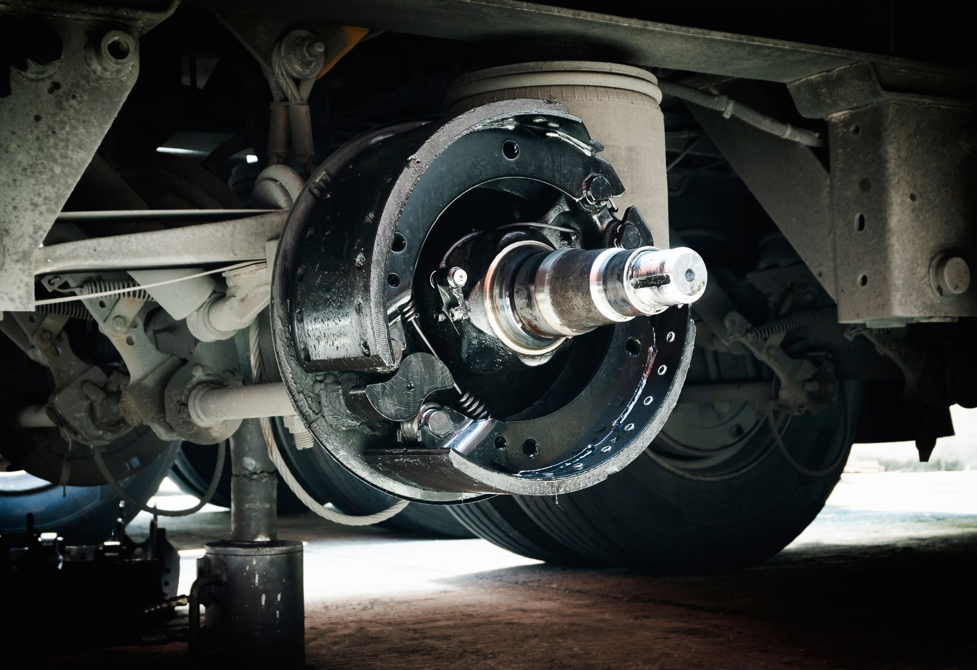 Close-up of a truck wheel hub with removed brake drum, revealing brake shoes and axle components in a garage setting.