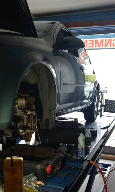 A dark-colored car elevated on a mechanic’s lift in a workshop, with the front tire removed for maintenance.